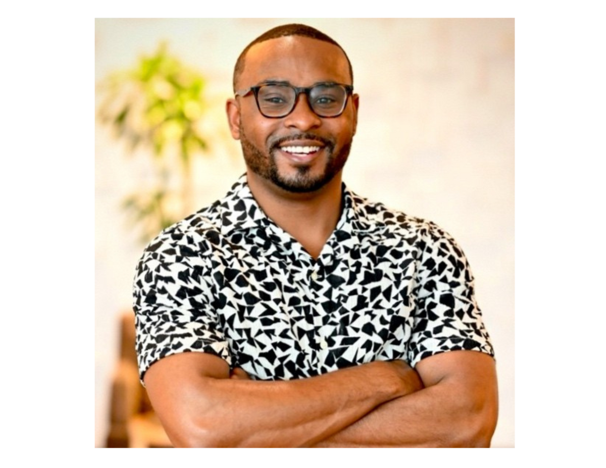 Man wearing a black and white patterned shirt with arms crossed against a blurred indoor background